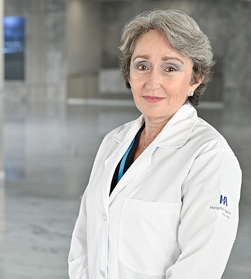 Es la foto de perfil de una otorrinolaringóloga en Querétaro de Hospital Angeles Centro Sur. Usa un suéter tejido de color amarillo con negro y verde, tiene dos collares largos, el cabello corto y canoso. está sonriendo.