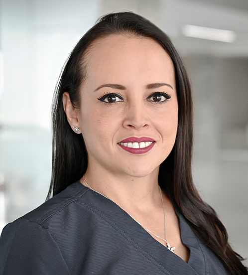 Es la foto de perfil de una ortopedista y traumatóloga en Querétaro de Hospital Angeles Centro Sur. Tiene un uniforme negro, con un collar plateado, está sonriendo, su cabello es largo y oscuro y es de tez morena.