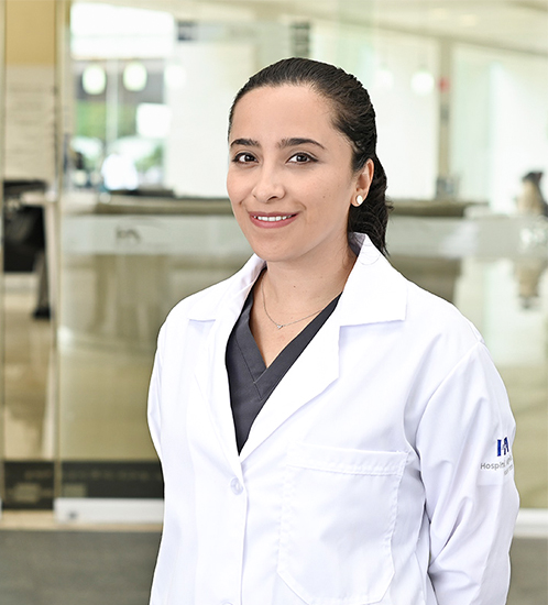 Es la foto de perfil de una oncóloga médica en Ciudad de México de Hospital Angeles Acoxpa. Usa una bata blanca con un uniforme médico color gris. Tiene el cabello negro y recojido en una coleta.