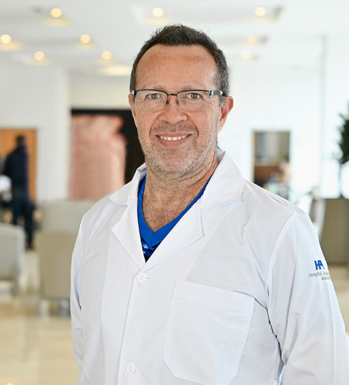 Experimentado médico anestesiólogo del Hospital Angeles Xalapa posa sonriente usando lentes y bata blanca en el lobby del hospital.