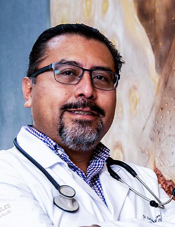 Es la foto de perfil de un infectólogo en León de Hospital Angeles León. Usa una bata blanca con camisa a cuadros, tiene lentes y bigote y barba.