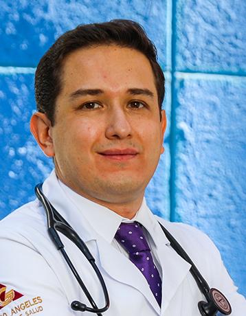 Es la foto de perfil de un pediatra especialista en ecocardiografía y cardiología pediátrica en León de Hospital Angeles León. Utiliza una bata blanca con una camisa blanca y una corbata morada. Tiene un estetoscopio sobre los hombros. 