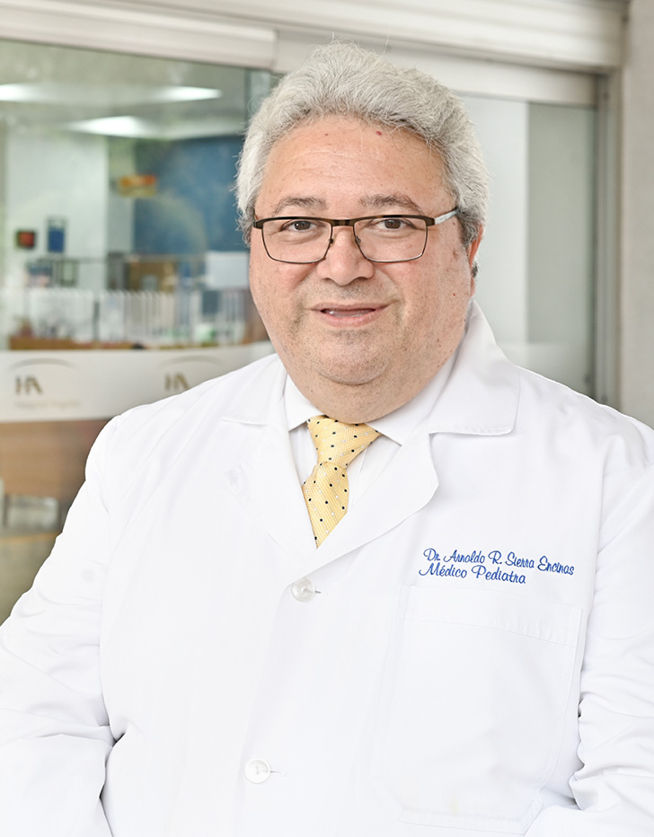 Es la foto de perfil de un pediatra en Tijuana de Hospital Angeles Tijuana. Usa una bata blanca y una corbata de cuadros amarillo con azul. Tiene el cabello gris y usa lentes.