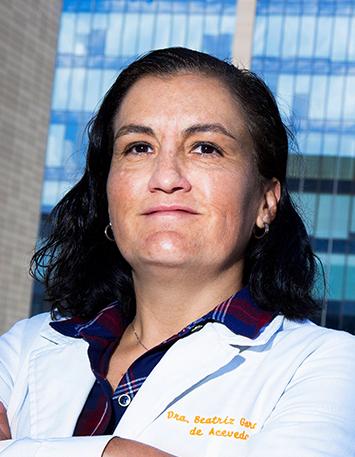 Es la foto de perfil de una dermatóloga en Ciudad de México de Hospital Angeles Pedregal. Usa una bata blanca y una blusa azul. Tiene el cabello corto negro y está sonriendo.