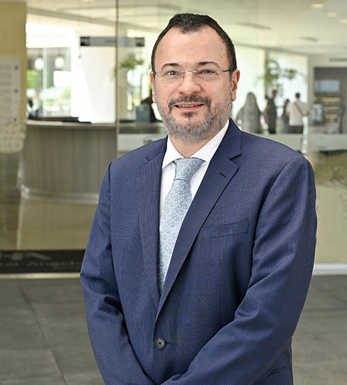 Es la foto de perfil de un ginecólogo y obstetra en Ciudad de México de Hospital Angeles. El doctor tiene un uniforme azul rey y de fondo una playera blanca, tiene lentes y de fondo se encuentra el hospital.