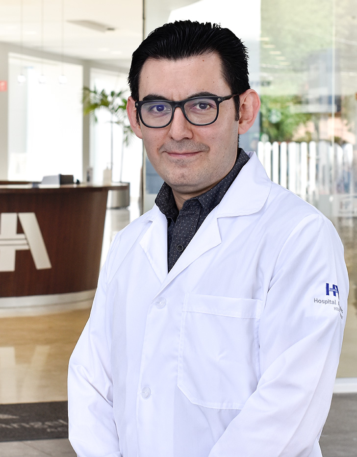 Es la foto de perfil de un geriatra en Ciudad de México de Hospital Angeles Acoxpa. Usa una bata blanca con una camisa negra. Tiene puesto lentes y tiene el cabello de color negro.