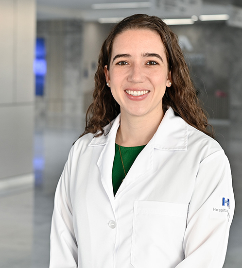 Es la foto de perfil de una pediatra en Querétaro de Hospital Angeles Centro-sur. Tiene el cabello largo, castaño y chino. Usa un collar dorado y aretes de perla. Tiene puesto una bata blanca y una blusa verde.