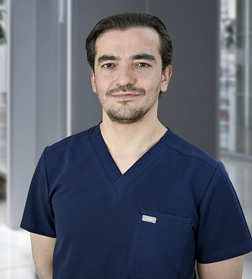 Es la foto de perfil de un oftalmólogo en Huixquilucan de Hospital Angeles Lomas. Tiene una bata blanca, y debajo de la bata tiene un suéter negro con camisa blanca. Su cabello está debajo de sus orejas y es castaño claro.