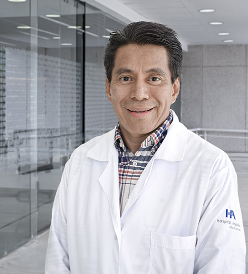 Es la foto de perfil de un dermatólogo en Villahermosa de Hospital Angeles Villahermosa. Usa una bata blanca y una camisa de cuadros blanco con azul. Tiene el cabello gris y está sonriendo.