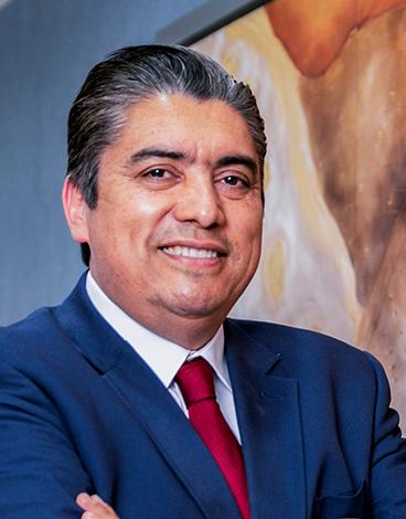 Es la foto de perfil de un cirujano oncológico en León de Hospital Angeles León. Utiliza un saco azul marino con camisa blanca y corbata roja. Tiene los brazos cruzados y está sonriendo.