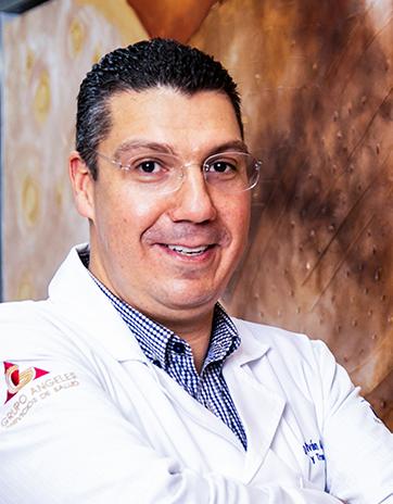 Es la foto de perfil de un ortopedista y traumatólogo en León de Hospital Angeles León. Usa bata blanca, camisa azul marino con rayas blancas y tiene lentes.