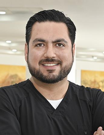 Es la foto de perfil de un ortopedista y traumatólogo en Ciudad Juárez de Hospital Angeles Ciudad Juárez. Usa un uniforme negro, tiene barba y está sonriendo. 
