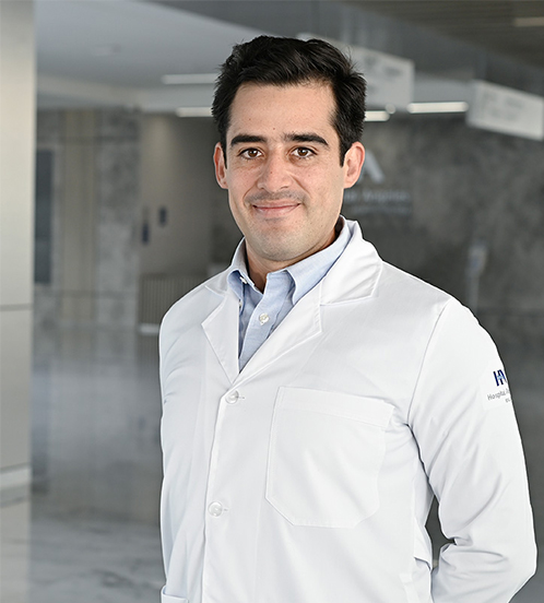 Es la foto de perfil de un infectólogo en Querétaro de Hospital Angeles Centro Sur. Se encuentra de pie. Trae puesto una bata blanca con una camisa color azul claro. Tiene el cabello azul oscuro.