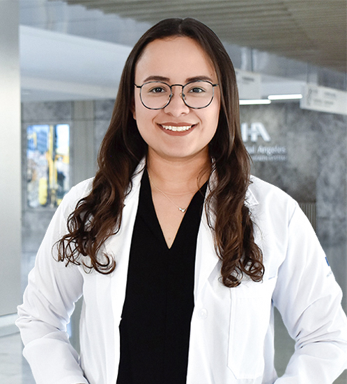 Es la foto de perfil de una coloproctóloga en Querétaro de Hospital Angeles Centro-sur. Tiene puesto una bata blanca con un uniforme médico color negro. Tiene el cabello largo y ondulado color castaño. Usa lentes negros y un collar plata.