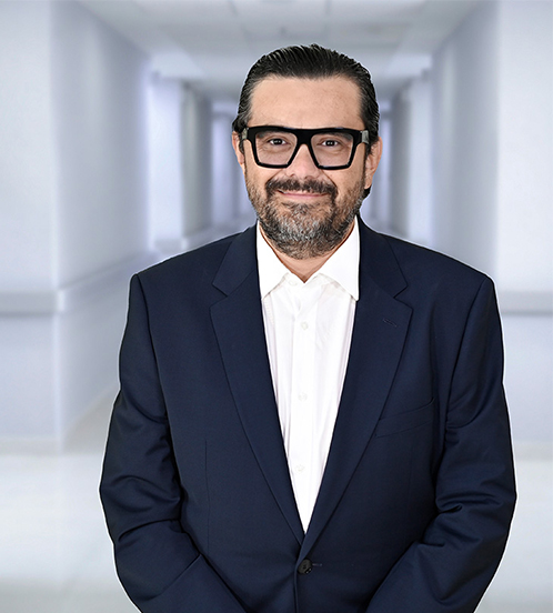 Es la foto de perfil de un urólogo en Ciudad Juárez de Hospital Angeles Ciudad Juárez. Tiene un traje azul con cuadros, camisa azul claro y está sonriendo. Tiene cabello oscuro.