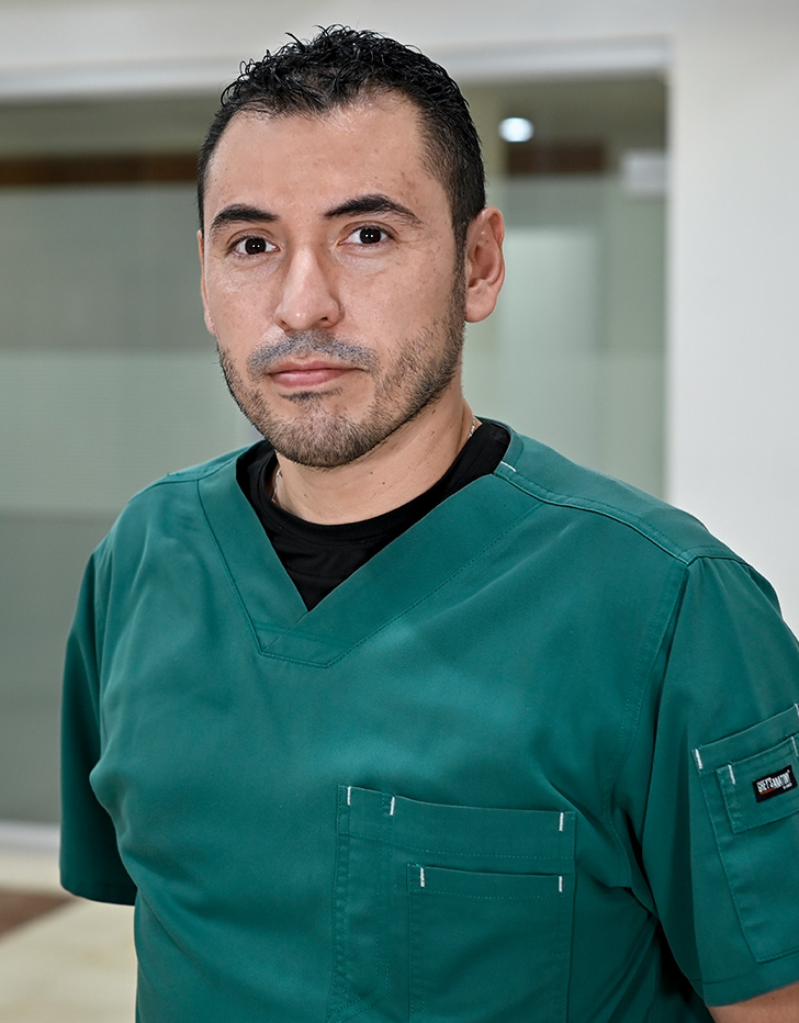 Es la foto de perfil de un infectólogo e internista en Ciudad de México de Hospital Angeles Mocel. Usa un uniform médico color verde con una camisa negra. Tiene el cabello y barba color negro. Sus brazos están cruzados por detrás.