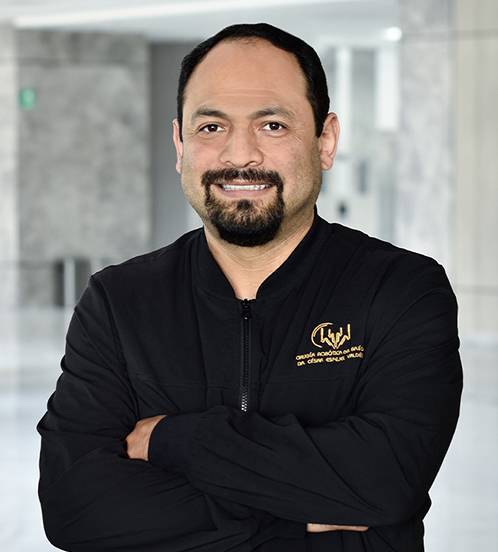 Es la foto de perfil de un cirujano oncológico en Querétaro de Hospital Angeles Centro Sur. Utiliza una chamarra con letras bordadas doradas, es de tez morena, tiene barba de candado y está sonriendo.