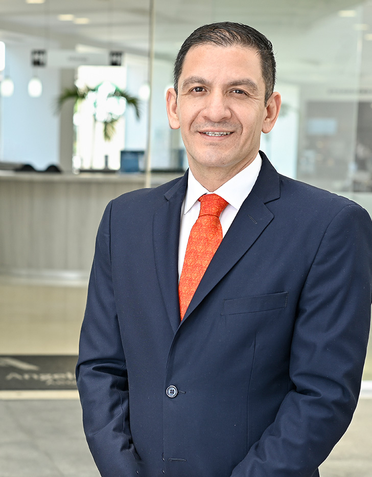 Es la foto de perfil de un cirujano general en Ciudad de México de Hospital Angeles. Tiene un uniforme azul rey, está sonriendo a la cámara, es de tez morena y cabello oscuro.