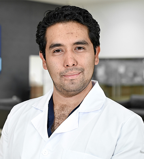 Es la foto de perfil de un cirujano general en San Luis Potosí de Hospital Angeles San Luis Potosi. Usa una bata blanca con un uniforme médico color negro. Su cabello es negro.