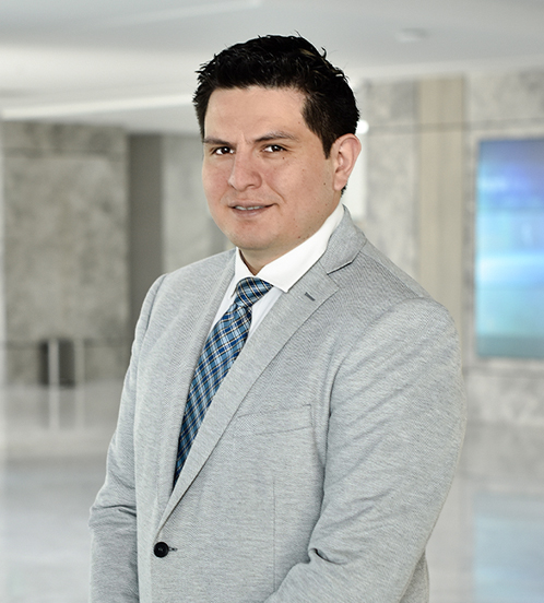 Es la foto de perfil de un cirujano general en Querétaro de Hospital Angeles Centro Sur. Usa un saco gris, una camisa blanca y una corbata azul con cuadros.