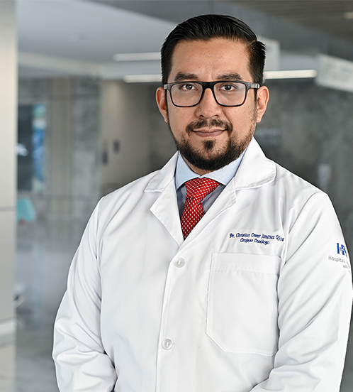 Es la foto de perfil de un cirujano oncológico en Querétaro de Hospital Angeles Centro Sur. está sonriendo, tiene lentes y barba. Usa un uniforme negro.