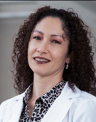 Es la foto de perfil de una ginecóloga y obstetra en Huixquilucan de Hospital Angeles Lomas. Usa una bata blanca con una blusa blanca con manchas negras. Su cabello es rizado y es de tez blanca.