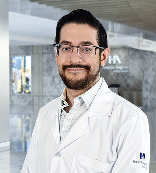 Es la foto de perfil de un cardiólogo en Querétaro de Hospital Angeles Centro-sur. Usa una bata blanca, con una camisa blanca de cuadros. Tiene el cabello y barba café oscuro. Está sonriendo ligeramente.
