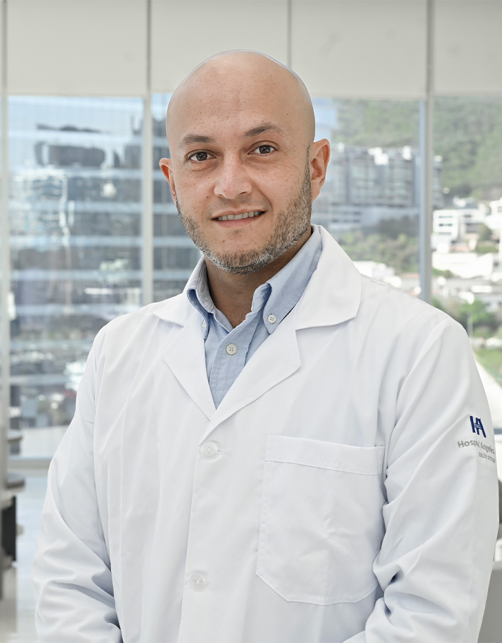 Es la foto de perfil de un algólogo y anestesiólogo en San Pedro Garza García de Hospital Angeles Valle Oriente. Usa una bata color blanco con una camisa de color azul claro. Es calvo y tiene la barba gris. Está sonriendo.
