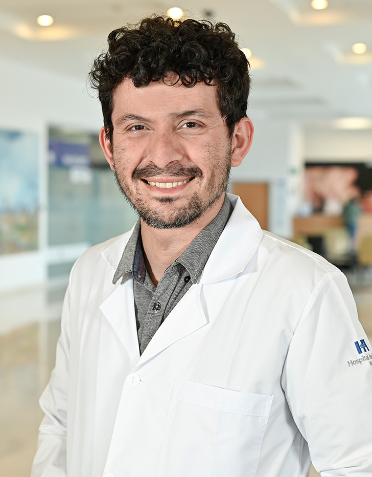 Es la foto de perfil de un médico internista y nefrólogo en Xalapa de Hospital Angeles Xalapa. Usa un uniforme médico color azul. Tiene el cabello chino y café oscuro.