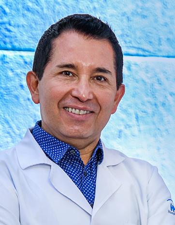 Es la foto de perfil de un pediatra en León de Hospital Angeles León. Usa una bata blanca, camisa azul y está sonriendo.