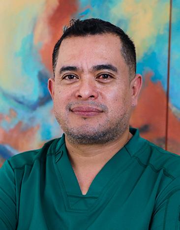 Es la foto de perfil de un urólogo en Tampico de Hospital Angeles Tampico. Usa un unidorme médico color verde. Tiene el cabello negro y los brazos cruzados.