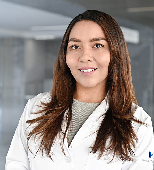 Es la foto de perfil de una ginecóloga y obstetra en Querétaro de Hospital Angeles Centro Sur. Usa una bata blanca y un suéter color camel de cuello alto. Tiene lentes vino.