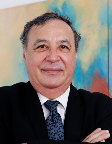 Es la foto de perfil de un ginecólogo y obstetra en Tampico de Hospital Angeles Tampico. Usa un saco negro, camisa blanca y corbata azul. Tiene el cabello gris. Tiene los brazos cruzados y está sonriendo.