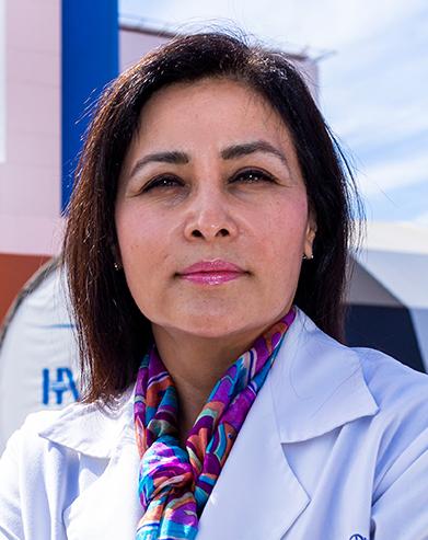 Es la foto de perfil de un pediatra en Tijuana de Hospital Angeles Tijuana. Usa una bata blanca y una blusa morada con flores. Tiene el cabello lacio y café-pelirrojo.