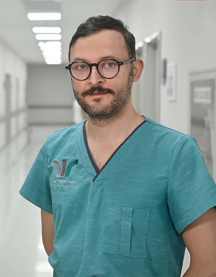 Es la foto de perfil de un urólogo en Ciudad de México de Hospital Angeles Universidad. Usa un uniforme médico color azul-verde y lentes redondos. Tiene el cabello, barba y bigote negro.