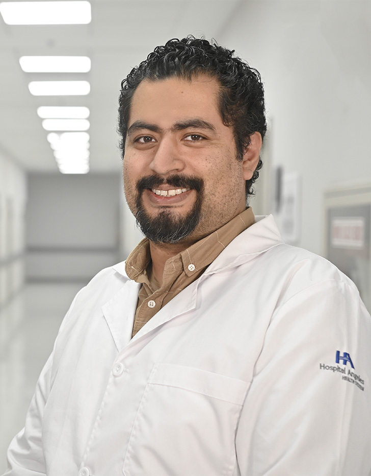 Es la foto de perfil de un médico internista en Ciudad de México de Hospital Angeles Universidad. Usa una bata blanca y camisa café. Tiene el cabello y braba negro.