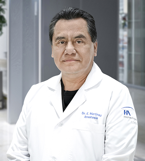 Es la foto de perfil de un anestesiólogo en Huixquilucan de Hospital Angeles Lomas. Usa una bata blanca, tiene camisa gris, es de tez morena y su cabello es negro.