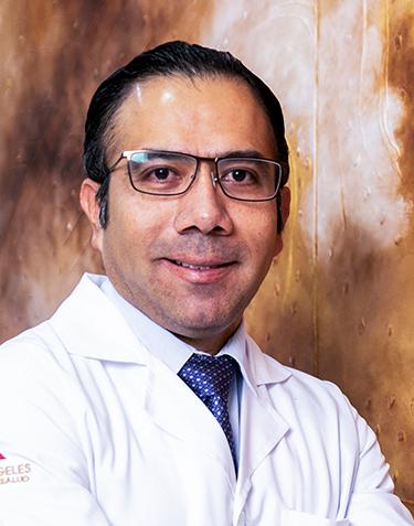 Es la foto de perfil de un ortopedista y traumatólogo en León de Hospital Angeles León. Usa una bata blanca con una camisa blanca y una corbata azul marino, tiene lentes.