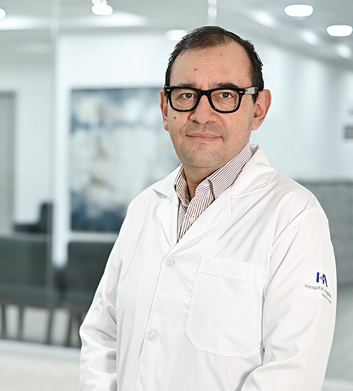 Es la foto de perfil de un cardiólogo en Ciudad de México de Hospital Angeles. Usa bata blanca con una camisa de rayas blancas con café claro. Usa lentes negros.