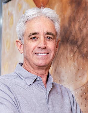 Es la foto de perfil de un ortopedista y traumatólogo en León de Hospital Angeles León. Utiliza una camisa gris, tiene el cabello canoso y está sonriendo.