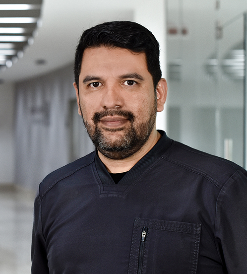 Es la foto de perfil de un pediatra y neonatólogo en Huixquilucan de Hospital Angeles Lomas. Tiene barba y bigote, está sonriendo y está parado en un pasillo del hospital. 