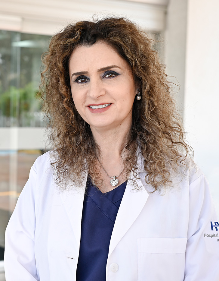 Es la foto de perfil de una ginecóloga oncológica en Tijuana de Hospital Angeles Tijuana. Usa una bata blanca. Tiene el cabello largo y café. Está sonriendo.