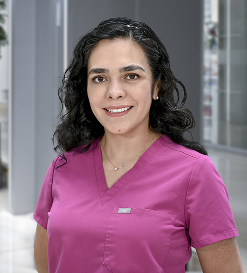 Es la foto de perfil de una otorrinolaringóloga en Huixquilucan de Hospital Angeles Lomas. Usa un saco blanco, tiene el cabello negro, largo y ondulado, y usa unos aretes circulares de color azul.