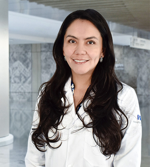 Es la foto de perfil de una médica general en Querétaro de Hospital Angeles Centro-sur. Usa una bata blanca con una blusa de flores con solores oscuros. Tiene el cabello largo y ondulado sonre sus hombros color café oscuro.