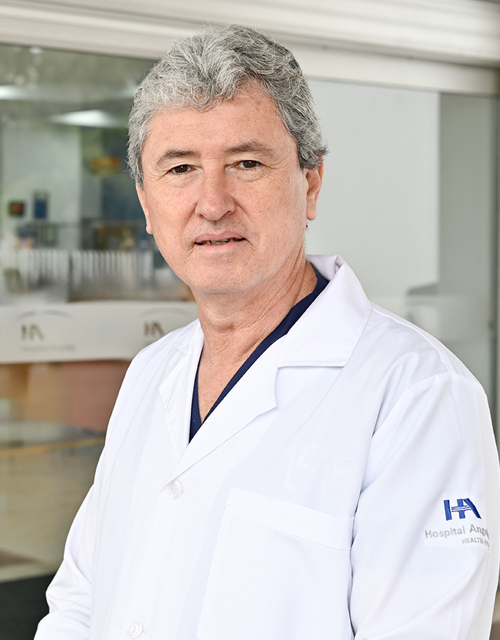 Es la foto de perfil de un urólogo en Tijuana de Hospital Angeles Tijuana. Usa una bata blanca y un uniforme médico azul. Tiene el cabello gris.