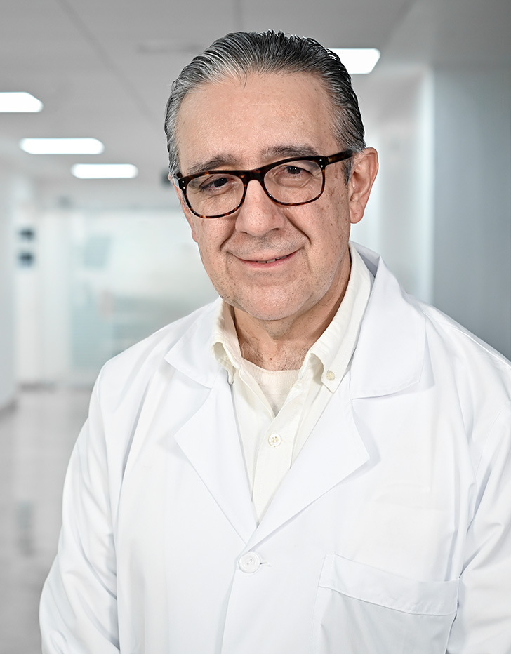 Es la foto de perfil de un infectólogo en Guadalajara de Hospital Angeles Del Carmen. Utiliza una bata blanca y una camisa azul. Tiene el cabello y la barba canosa.