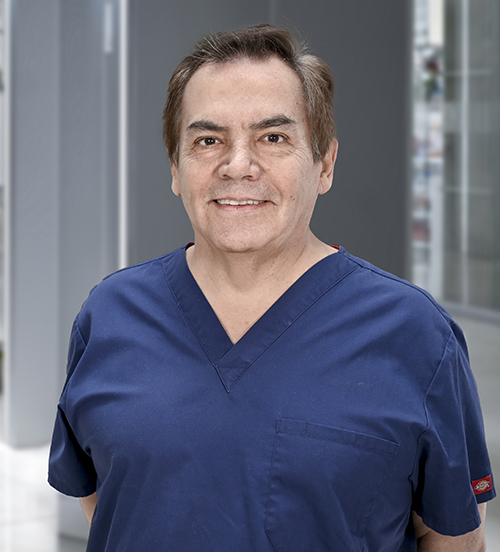 Es la foto de perfil de un cirujano plástico en Huixquilucan de Hospital Angeles Lomas. Usa un uniforme azul con cuello V, tiene los brazos cruzados.