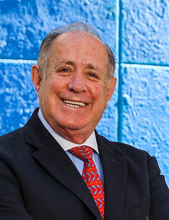 Es la foto de perfil de un cirujano general en León de Hospital Angeles León. Usa un traje negro, corbata roja y camisa azul cielo. está sonriendo amablemente.