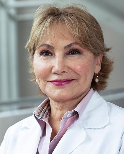 Es la foto de perfil de una dermatóloga en Huixquilucan de Hospital Angeles Lomas. Usa una bata blanca, camisas lila, tiene el cabello corto y rubio, está sonriendo.