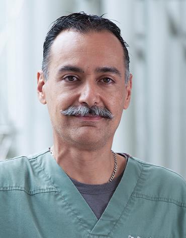 Es la foto de perfil de un pediatra en Huixquilucan de Hospital Angeles Lomas. Usa un uniforme de color verde con cuello V, tiene bigote y es canoso.